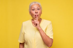 Kobieta w średnim wieku przykłada palec do ust w geście "cicho"