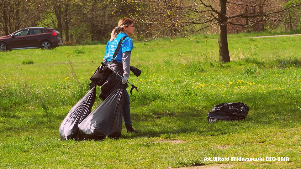 Młoda kobieta ciągnie po trawie worki ze śmieciami